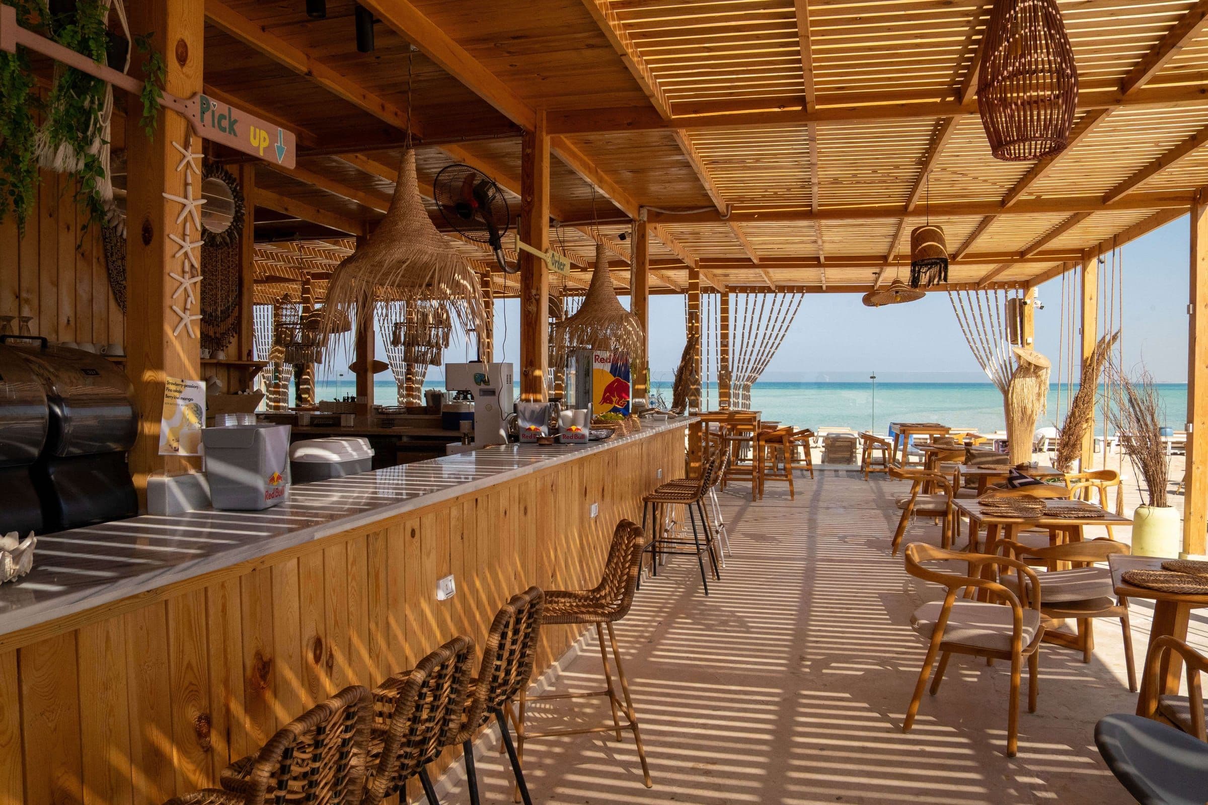 The bar counter under the wooden pergola, woven pendant lamps overhead and stools along the front