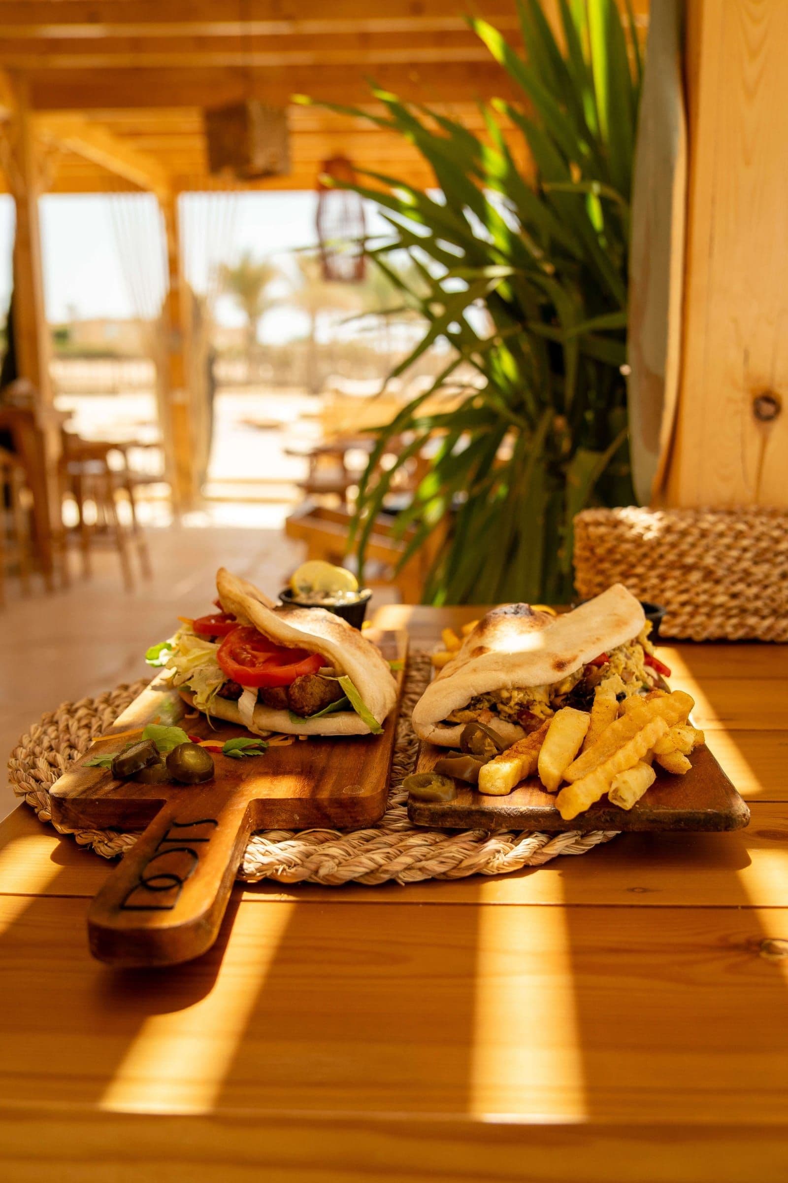 Two open sandwiches and fries served on a wooden board on a sunlit table
