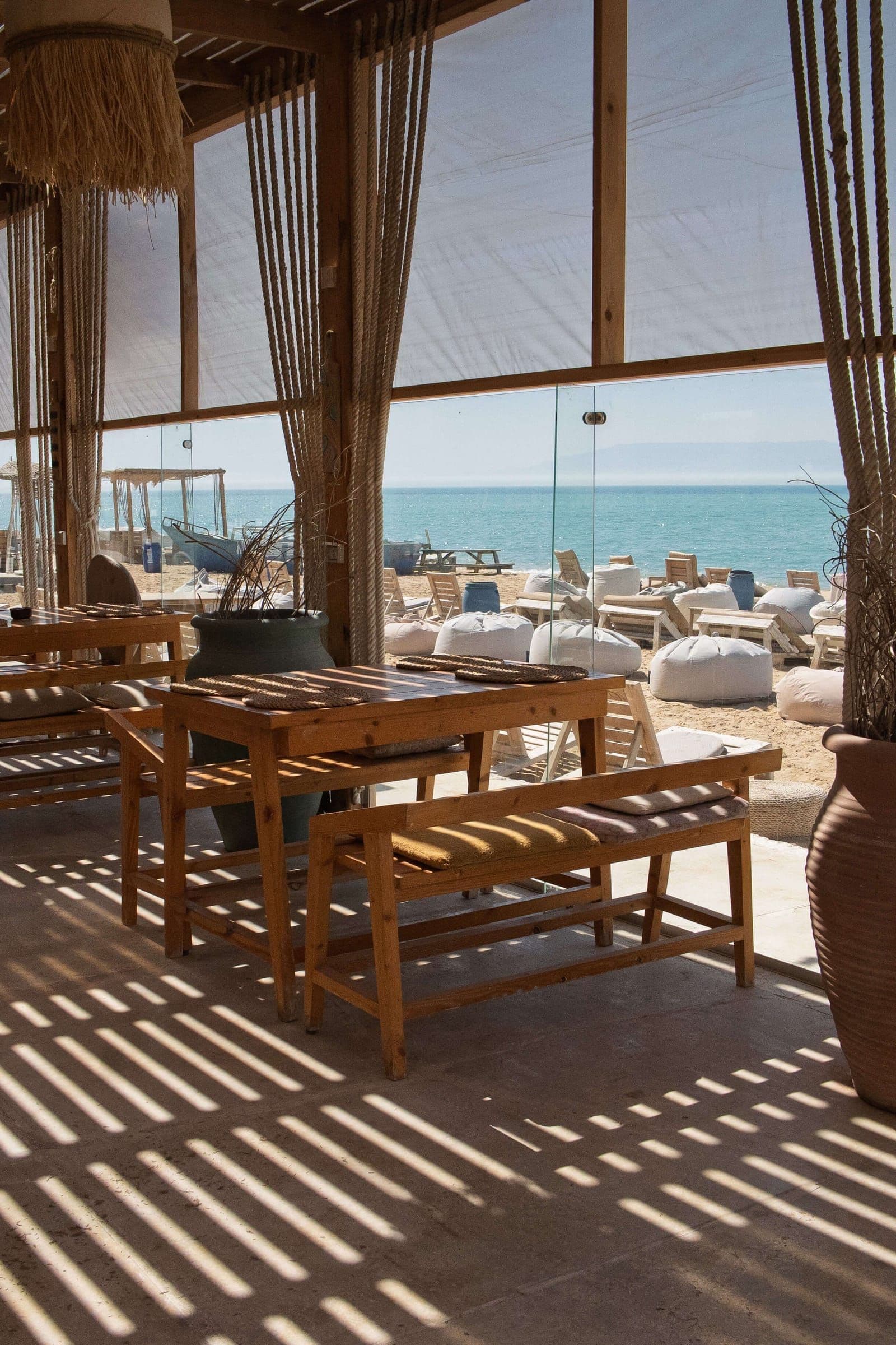 The sea framed by the beach club's glass front, with bean bags and sun loungers on the sand outside
