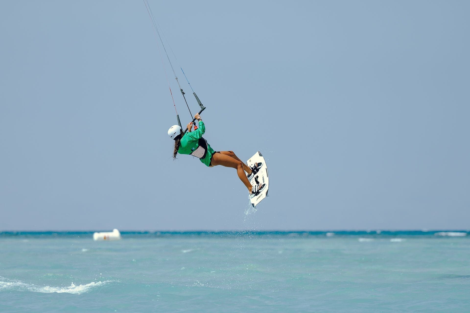 A kitesurfer high above the turquoise lagoon, mid-jump with the board angled out behind them