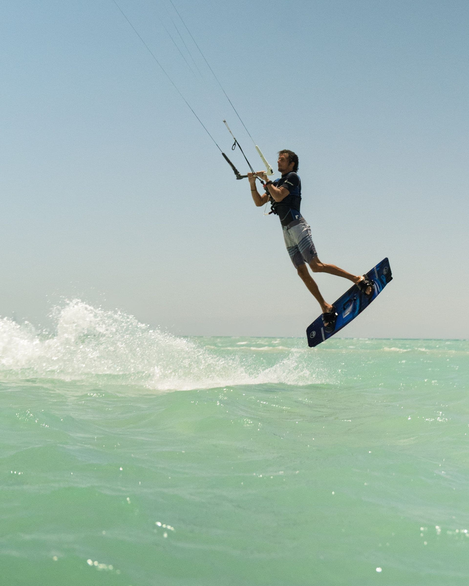 A kitesurfer jumps above pale turquoise water.